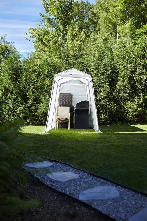 Un abri de rangement contenant du mobilier de jardin est apposé sur un terrain en gazon pour les protéger du soleil et des intempéries